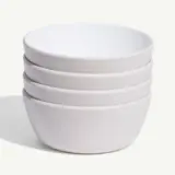 A stack of white ceramic bowls is neatly aligned against a plain background.