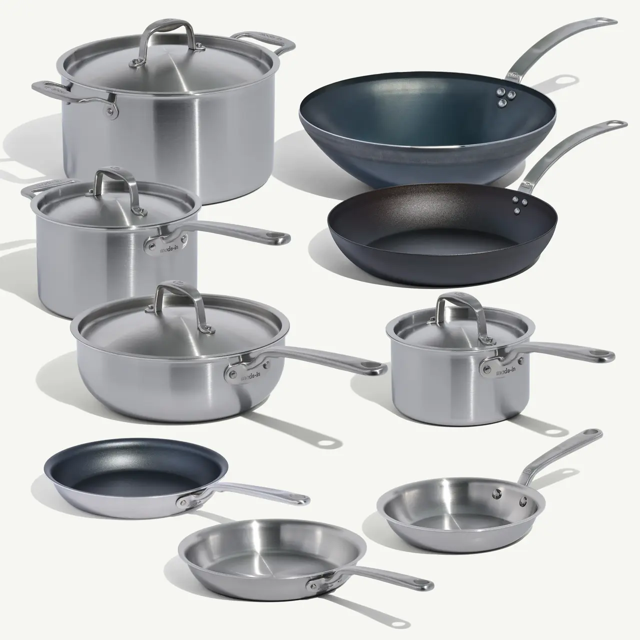 A variety of stainless steel pots and pans, including one non-stick skillet, arranged neatly against a light background.