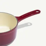 A deep red saucepan with a cream-colored interior and a red handle is shown.