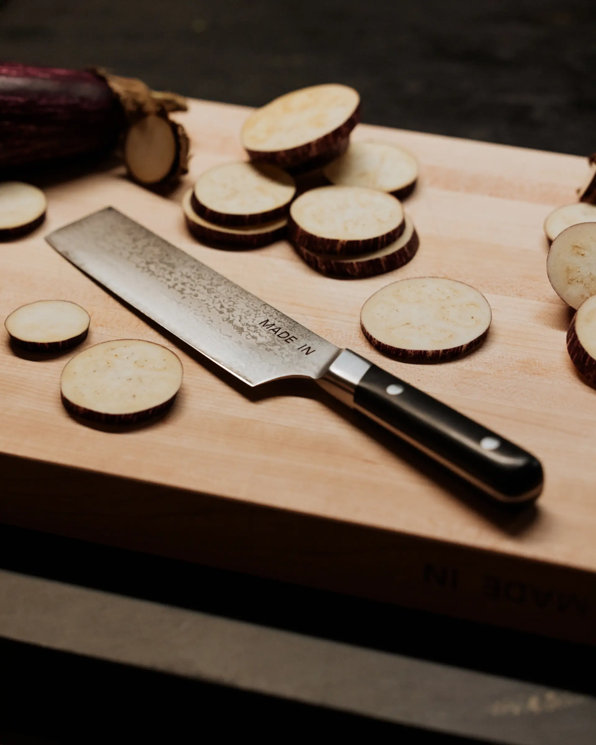 Sliced eggplants and a kitchen knife are arranged on a wooden cutting board.