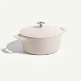 A round, cream-colored enameled cast-iron pot with a matching lid and metal knob.