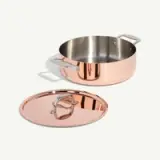 A shiny, stainless steel and copper pot with two handles is paired with a matching lid placed beside it.