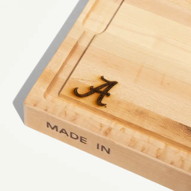 A wooden cutting board features a decorative letter "A" and the phrase "MADE IN" engraved on one side.