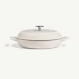 A round, light-colored cooking pot with a lid and two handles sits on a neutral background.