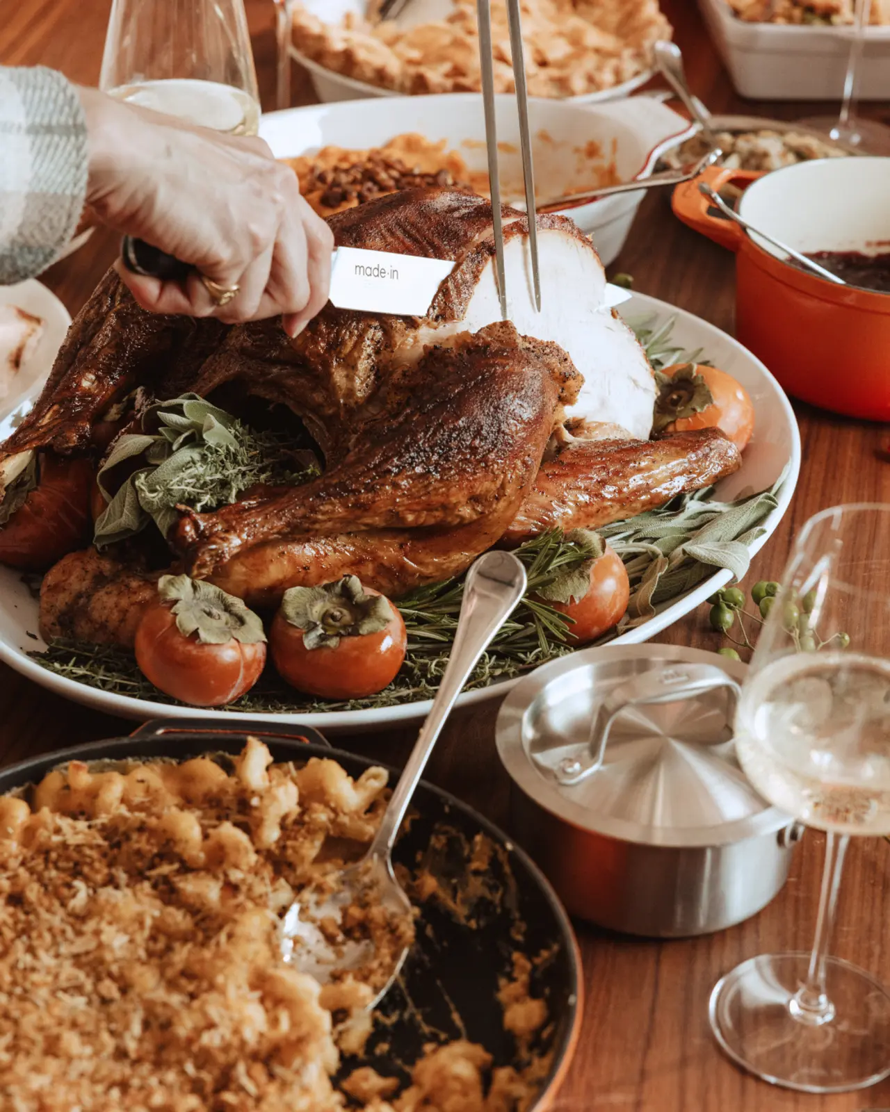 A person carves a roasted turkey surrounded by various dishes on a festive table setting.