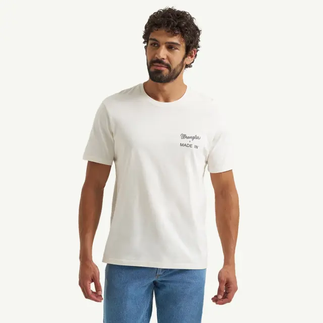 A man with curly hair is wearing a light-colored t-shirt featuring the words "Made In" in a stylish font.