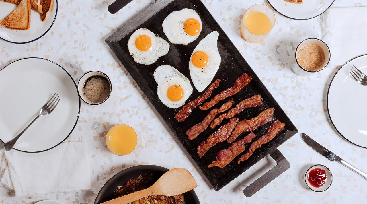 A breakfast spread featuring sunny-side-up eggs, bacon strips, toast, and various condiments neatly arranged on a table.
