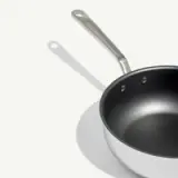 A non-stick frying pan with a metal handle casts a shadow on a light background.