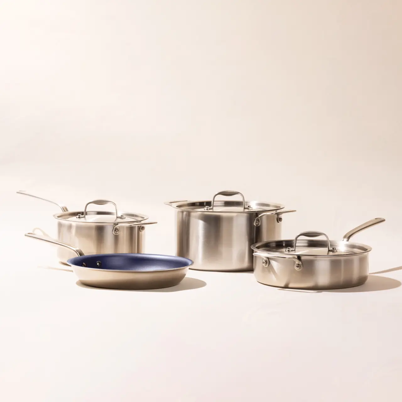A set of stainless steel cookware including pots and a pan with one blue interior, displayed against a light background.