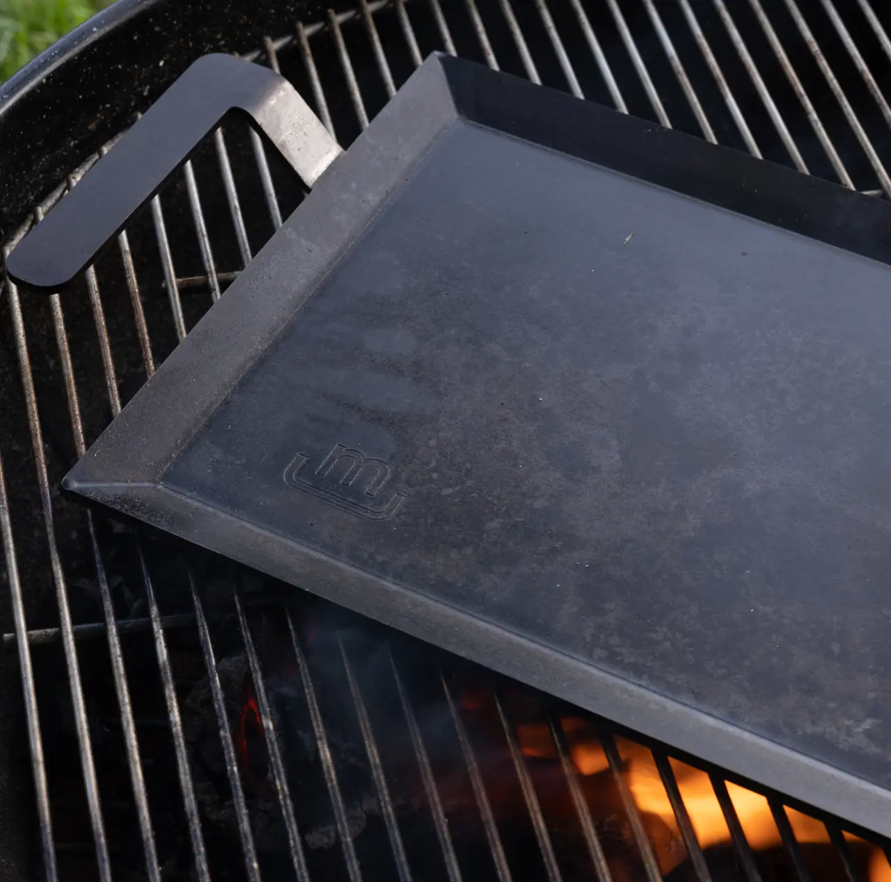 A cast iron griddle sits atop a grill with glowing embers beneath it, ready for cooking.