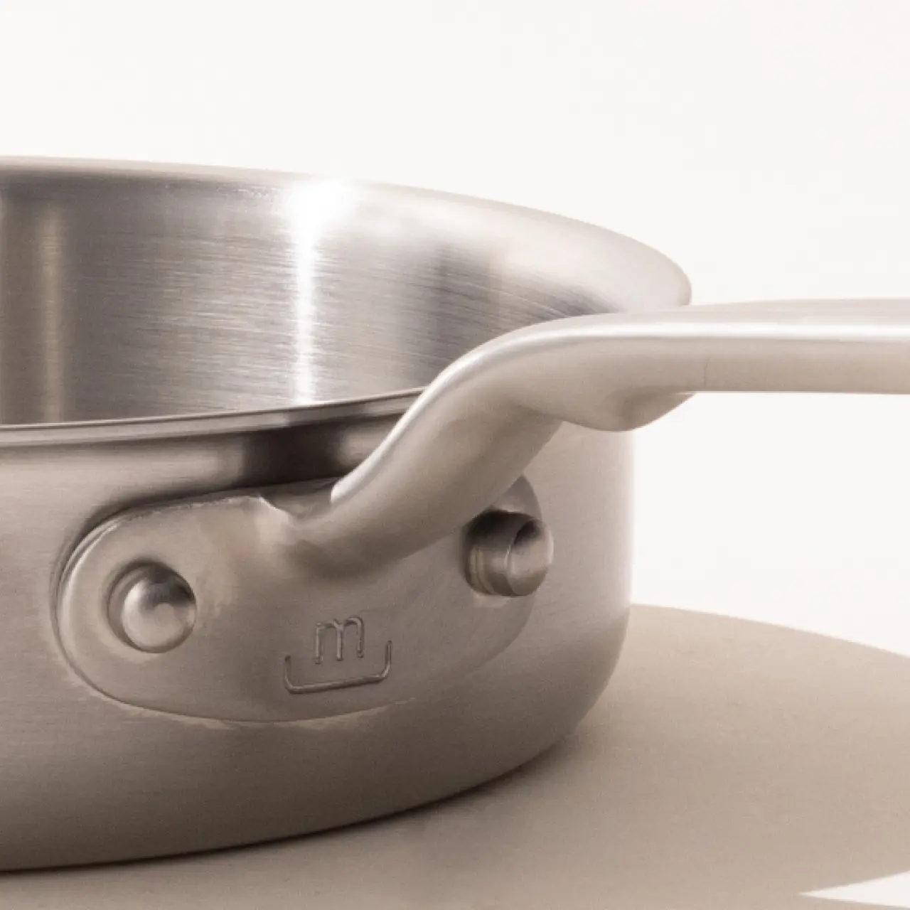 A stainless steel saucepan with a long handle on a neutral background.
