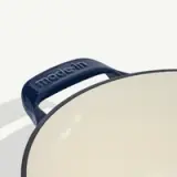 A close-up view of a cream-colored pan with a dark blue handle showing the brand name "madein."