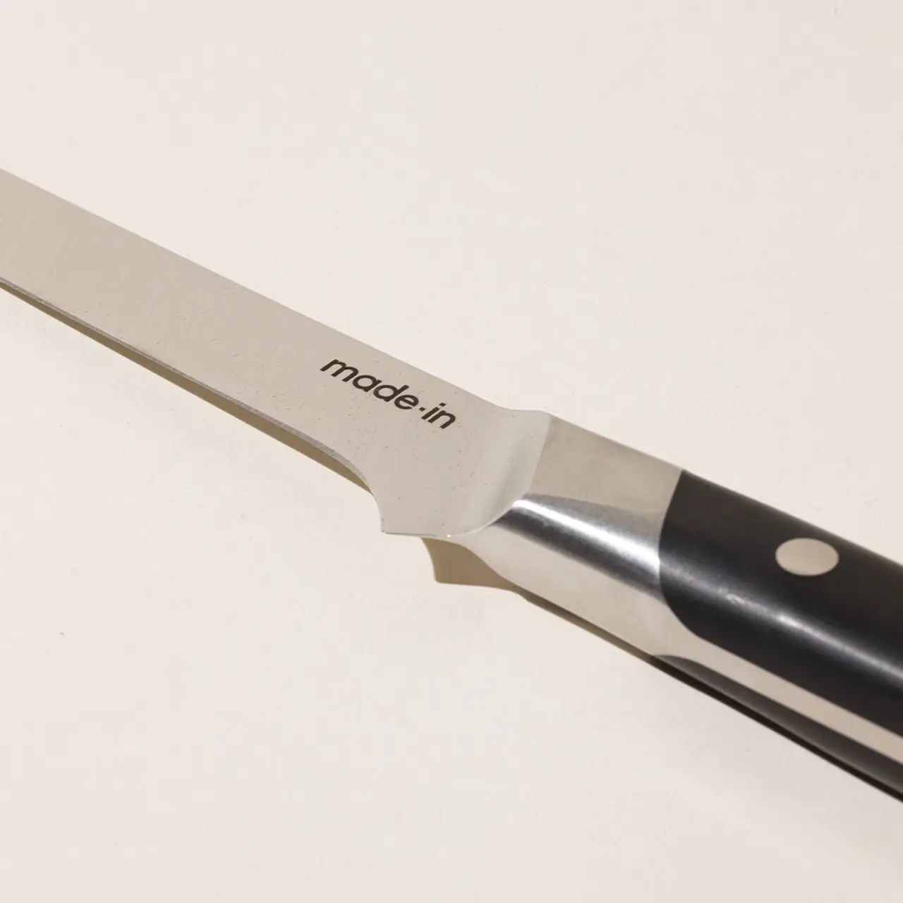 A close-up of a stainless steel kitchen knife with the inscription "made.in" on the blade, positioned against a plain background.