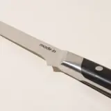 A close-up of a stainless steel kitchen knife with the inscription "made.in" on the blade, positioned against a plain background.