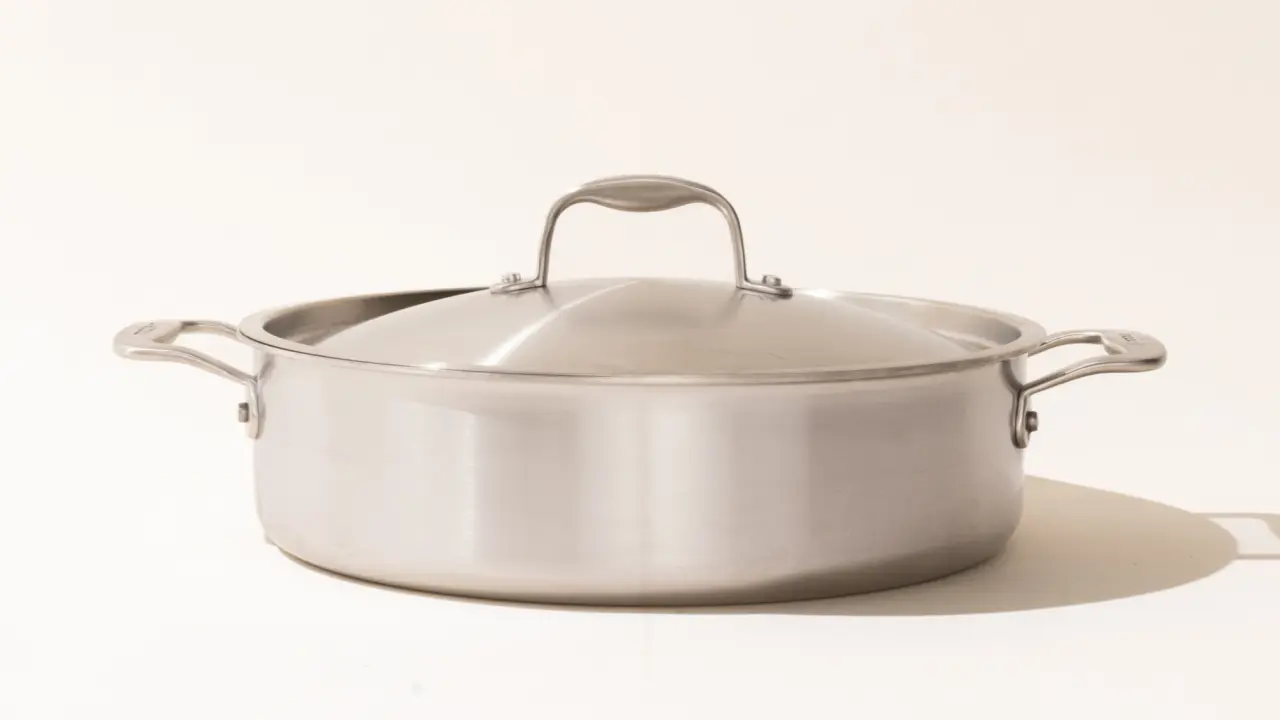 A stainless steel cooking pot with a lid on a light background.