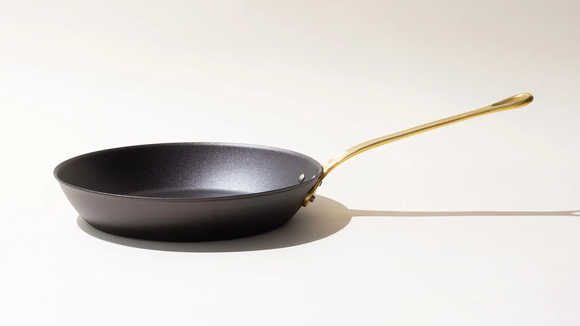 A black frying pan with a golden handle on a light background.