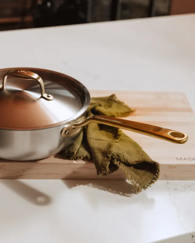 A stainless steel saucepan with a copper-colored handle sits on a marble countertop next to a folded green cloth.