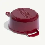 A glossy red enameled cast-iron pot is shown upside down, revealing its textured lid and handle.