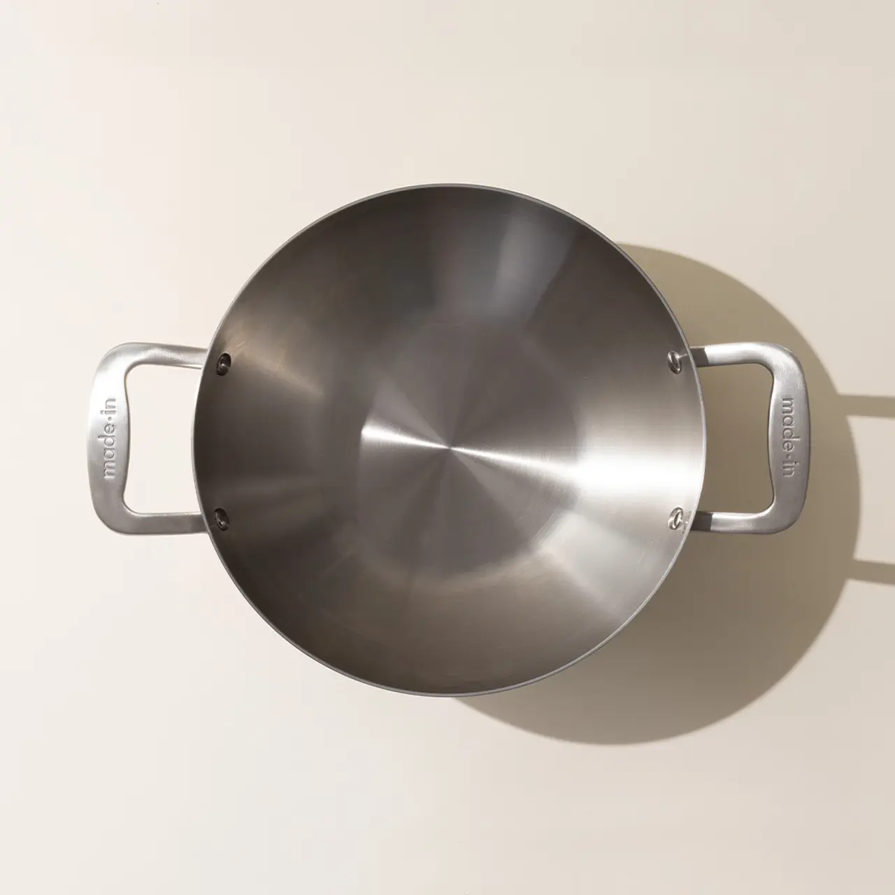 A stainless steel pot with two handles viewed from above on a neutral background.