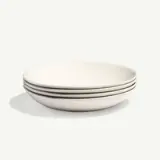 A stack of four white, round ceramic plates placed against a plain background.