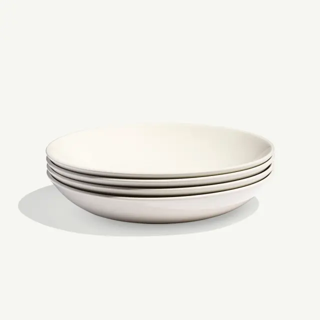 A stack of four white, round ceramic plates placed against a plain background.