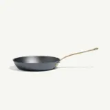 A black frying pan with a long gold-colored handle rests on a plain light background.
