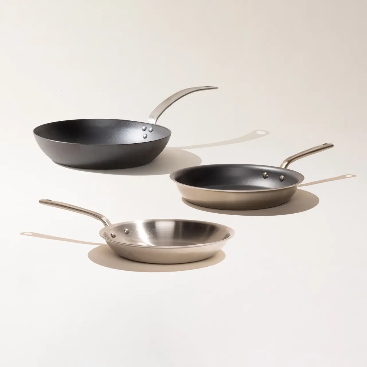 Three different-sized frying pans with varying finishes are neatly arranged in a descending row from left to right against a light background.