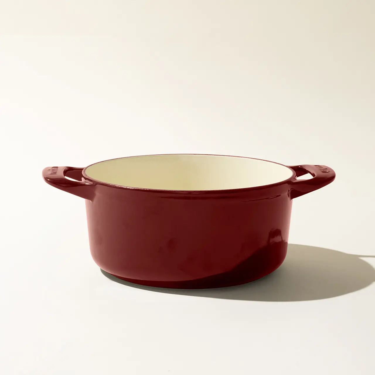 A red enameled cast iron Dutch oven with side handles on a neutral background.