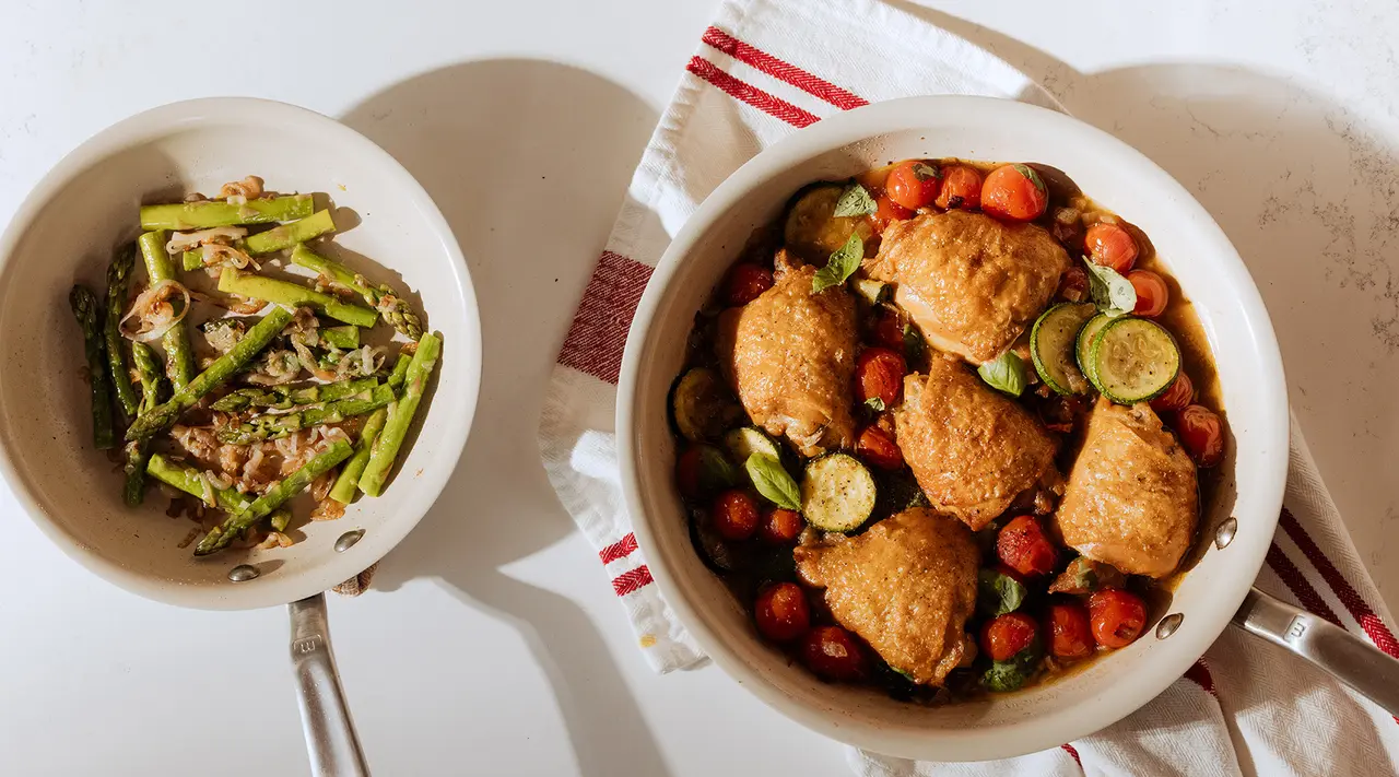 Two bowls on a table contain a salad with green beans and seeds, and a mix of fried chicken pieces with cherry tomatoes and zucchini slices, respectively, suggesting a prepared meal.