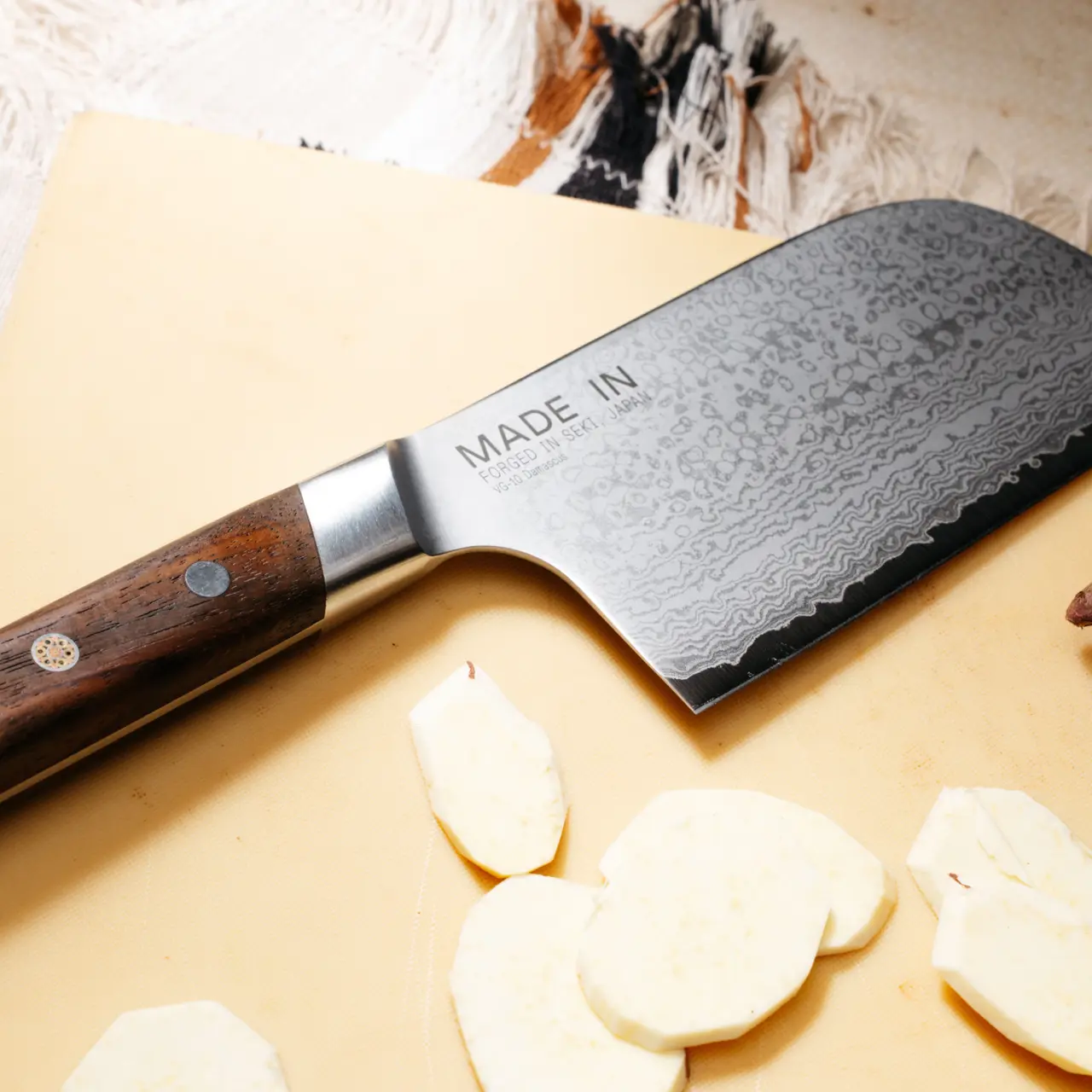 Made In Limited Edition Damascus Steel Kamagata 5" knife with a rosewood handle rests beside sliced garlic.