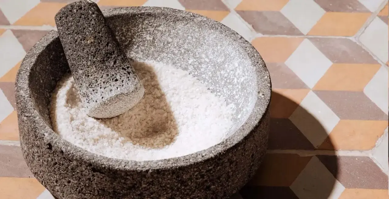 A stone mortar and pestle containing some ground white powder, set on a brown and beige tiled surface.