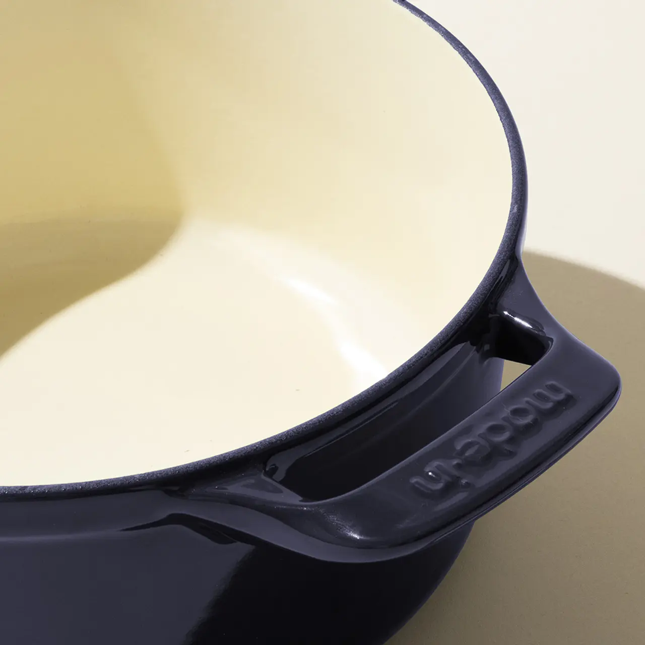 A close-up of a black and cream-colored Le Creuset pot showing the spout and brand name embossed on the handle.