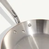 A stainless steel frying pan with a polished surface and riveted handle is shown against a white background.