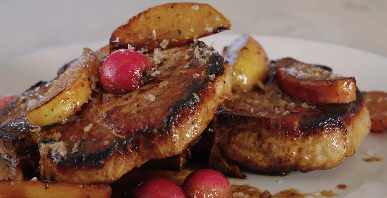 Seared pork chops accompanied by apples and red berries on a plate.