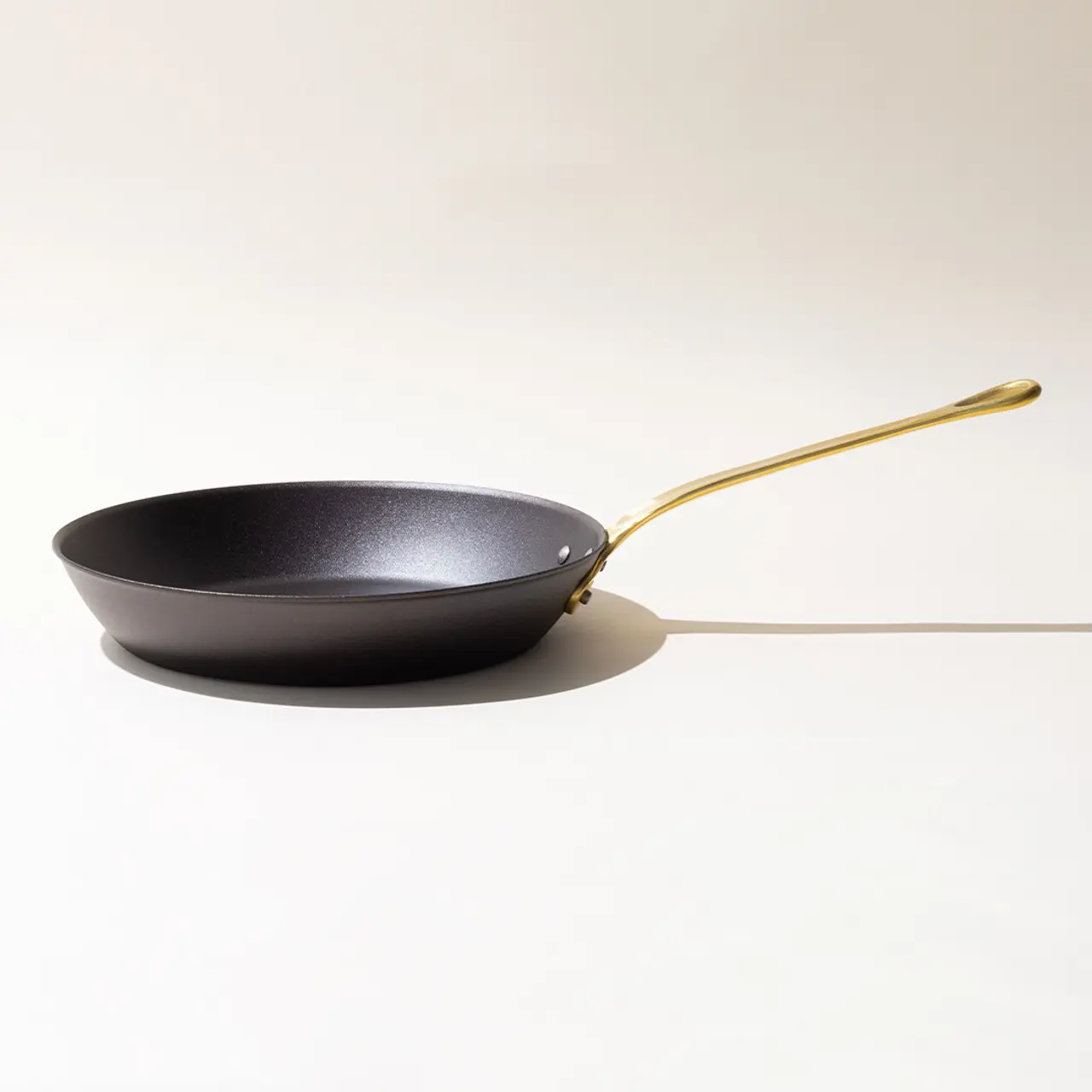 A black frying pan with a golden handle on a light background with a subtle shadow.