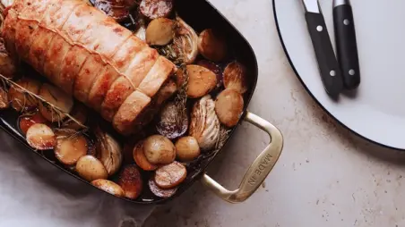 Porchetta with Spring Garlic, Fennel, and Potatoes roasts with browned potatoes in a Made In pan beside knives.