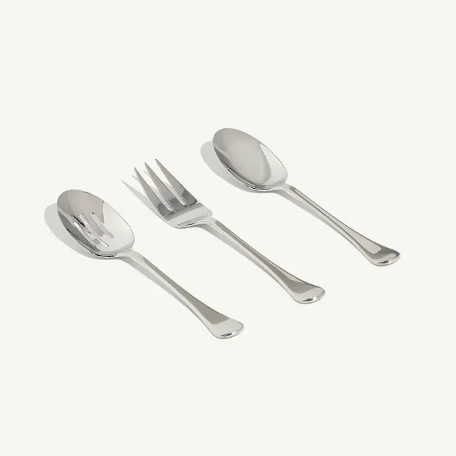 Three stainless steel utensils, including a serving spoon, serving fork, and soup spoon, are laid out on a plain background.