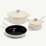 A set of three cream-colored cookware pieces including a lidded Dutch oven, a lidded saucepan, and a frying pan with a black interior.