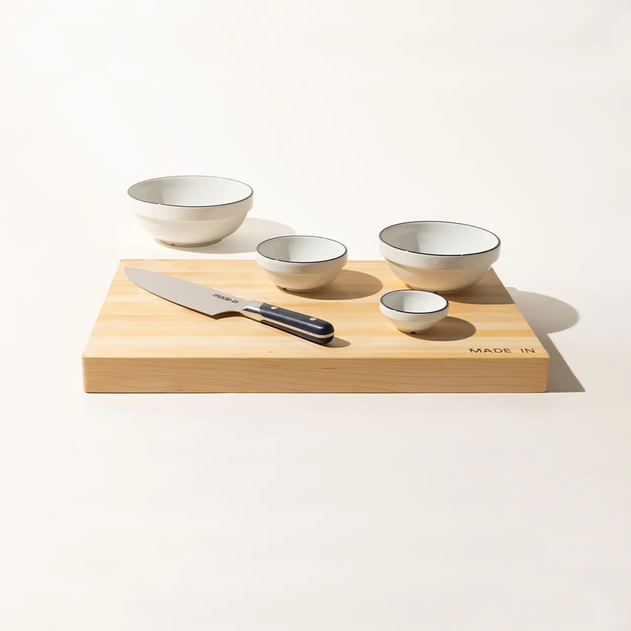 A kitchen knife and four varied-size bowls are neatly arranged on a bamboo cutting board with the text "MADE IN" visible.