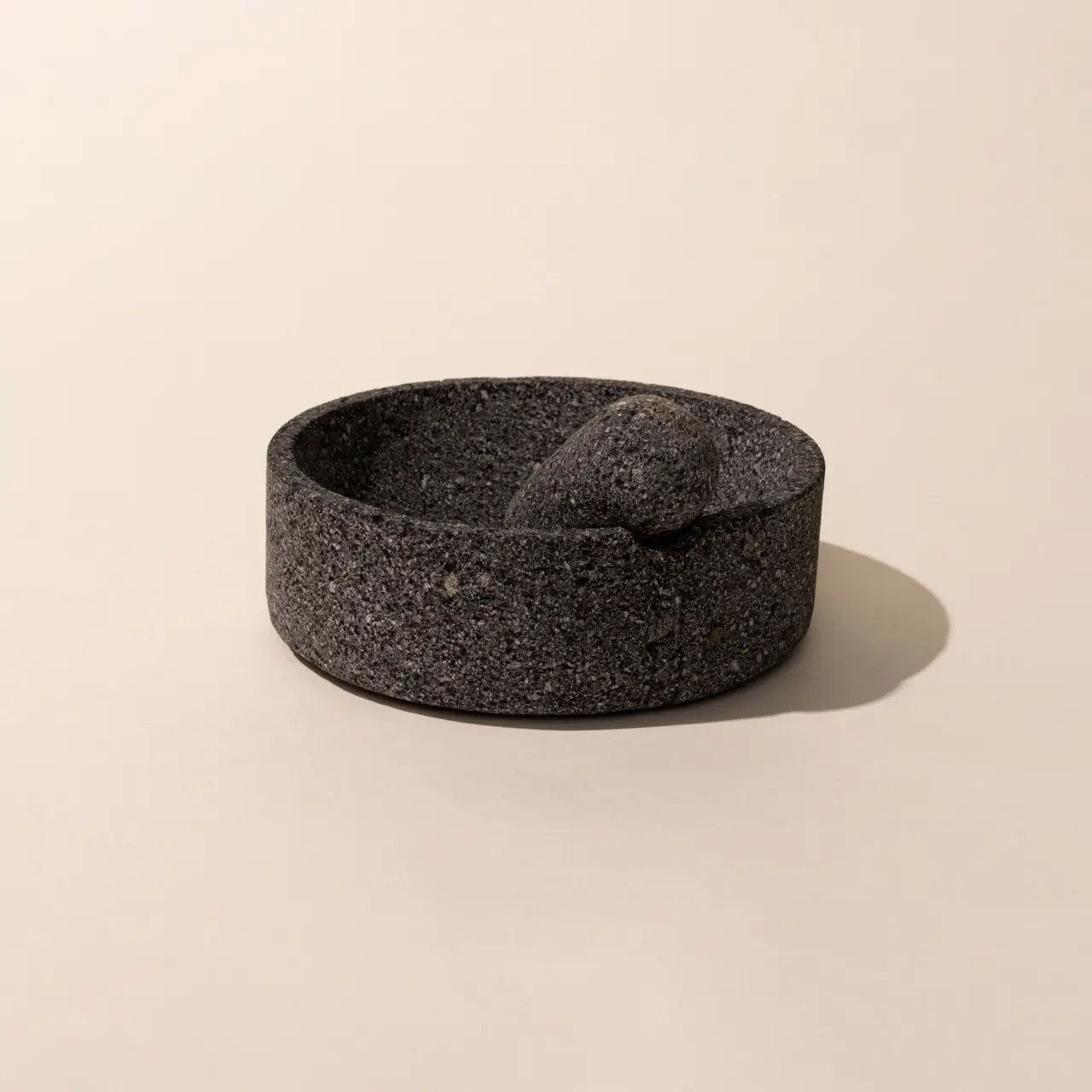 A stone molcajete, which is a traditional Mexican version of a mortar and pestle, on a neutral background.