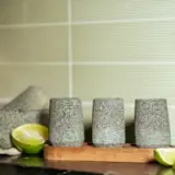 Three stone shot glasses are placed on a wooden tray with lime halves in the background.