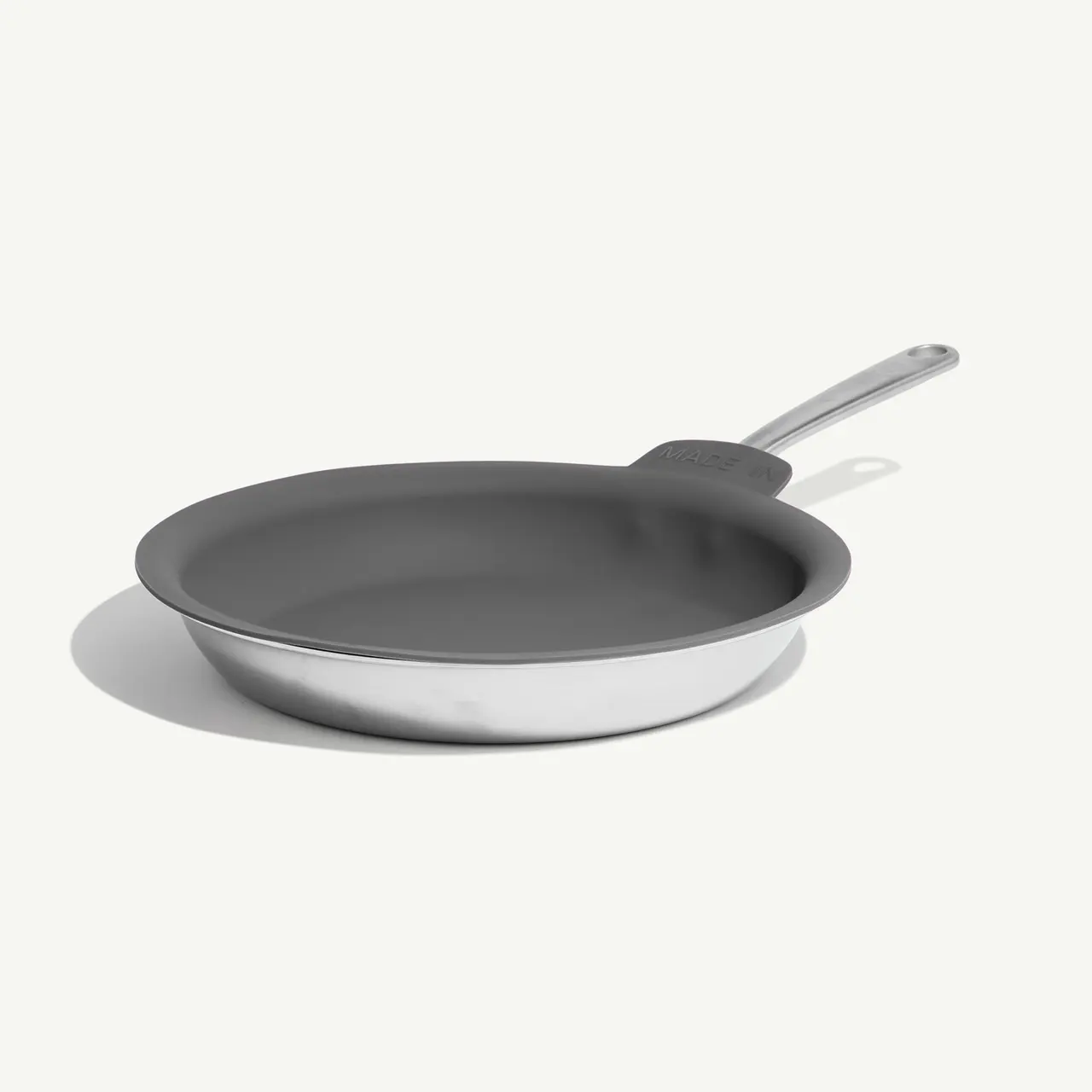 A stainless steel frying pan with a non-stick coating and a long handle rests on a plain background.