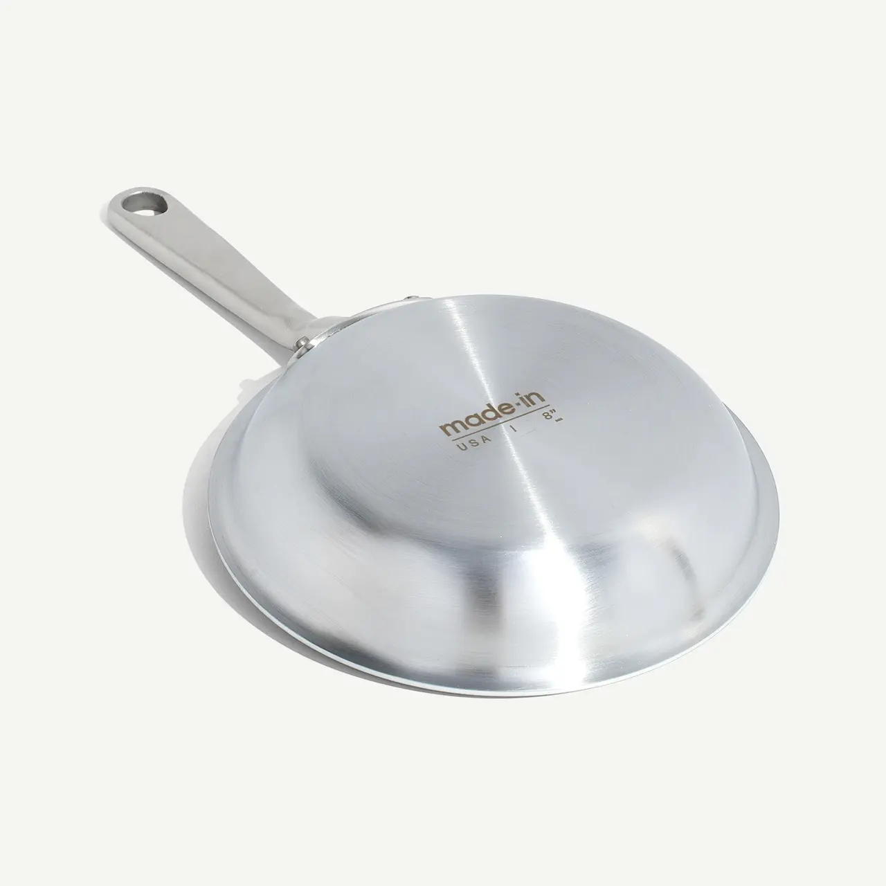 A stainless steel frying pan with a long handle presented against a light background, bearing the brand name 'made in'.