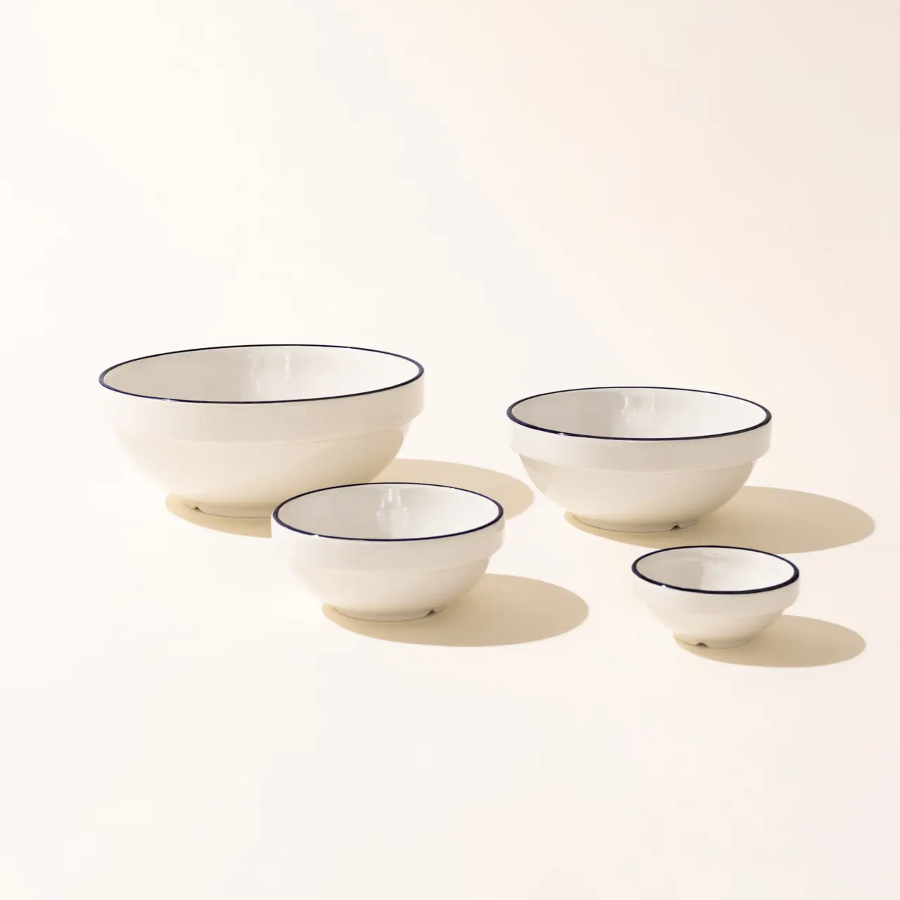 Four white ceramic bowls with navy blue rims are arranged in descending size order on a light background.