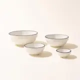 Four white ceramic bowls with navy blue rims are arranged in descending size order on a light background.