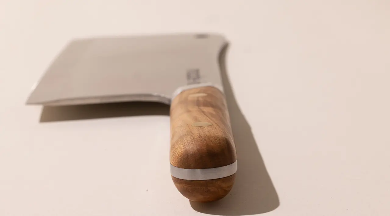 A stainless steel cleaver with a wooden handle on a light background.