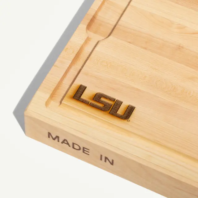 A wooden cutting board features the engraved letters "LSU" and the text "MADE IN" on one side.