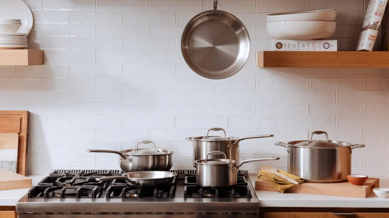 A well-organized kitchen counter with a variety of pots and a frying pan, a gas stove, and neatly arranged shelves against a tiled backsplash.