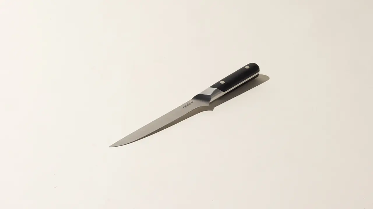 A kitchen knife with a black handle lies on a light-colored surface.