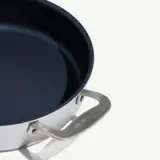 A close-up of a silver-handled frying pan on a white background showcases the pan's non-stick surface and branded handle.